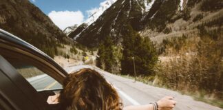 The bipolar express woman riding on vehicle putting her head and right arm outside the window while travelling the road