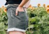 BEHIND woman standing on sunflower meadow holding pocket