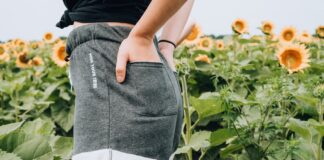 BEHIND woman standing on sunflower meadow holding pocket