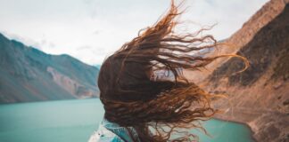 Blow Hard woman's hair covering her face near body of water