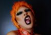 AFTER HOURS POETRY Naughty young ethnic androgynous guy with bright makeup in BDSM collar and wig embracing self and looking at camera with opened mouth