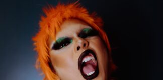 AFTER HOURS POETRY Naughty young ethnic androgynous guy with bright makeup in BDSM collar and wig embracing self and looking at camera with opened mouth